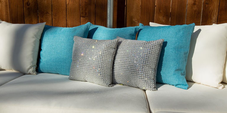 sofá exterior con cojines de diamantes de imitación y cojines turquesas en un patio con paneles de madera