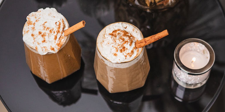 Lattes de especias de calabaza con bourbon, cubiertos con crema batida y palito de canela en tazas acogedoras de otoño