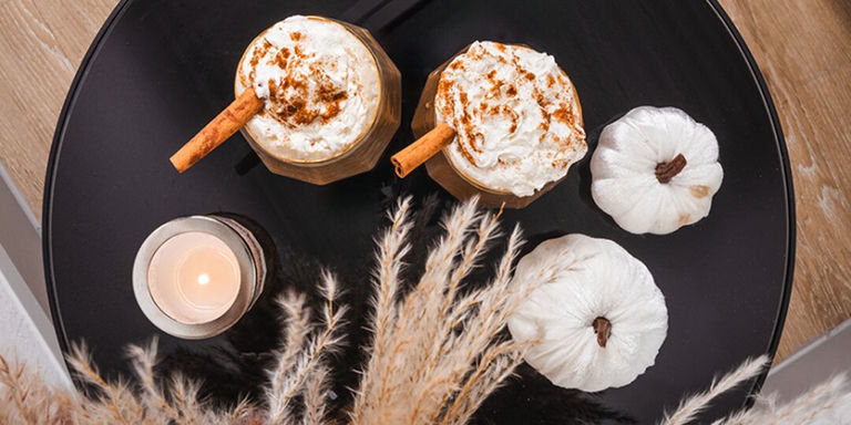Vista superior de lattes de especias de calabaza con crema batida y canela junto a calabazas blancas decorativas