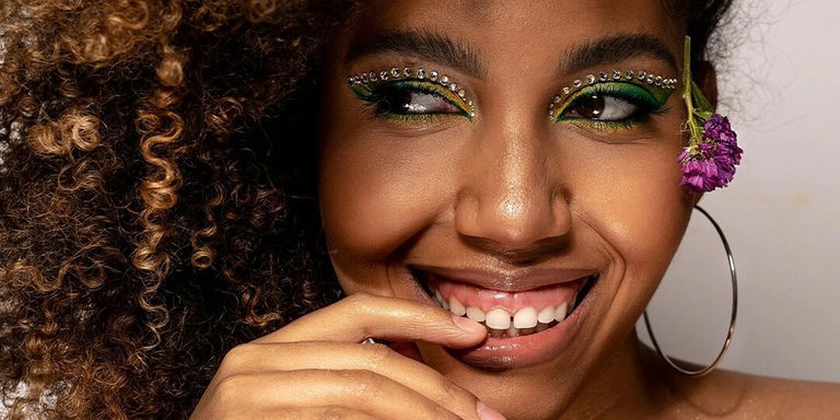Mujer sonriente con cabello rizado y sombra de ojos verde usando pedrerías con aplicación en caliente como detalle de delineador de ojos