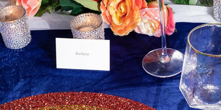 Glamorosa mesa de comedor en azul marino y oro con portavelas de pedrería y flores naranjas