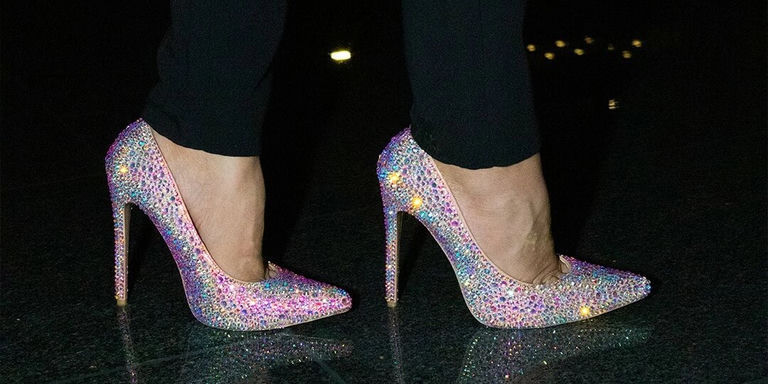 Primer plano de pies llevando tacones cubiertos de pedrería multicolor contra una superficie oscura de la calle