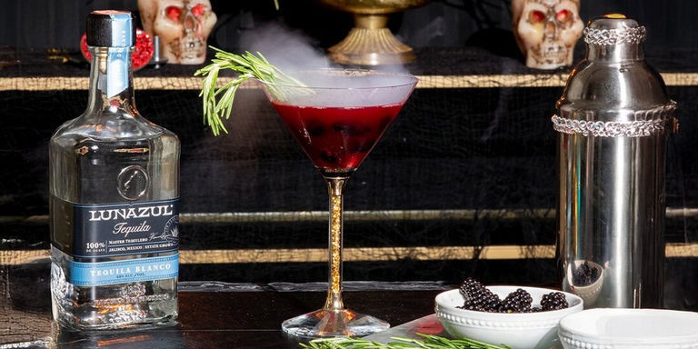 signature cocktail with rosemary garnish next to rhinestone shaker and blackberry garnish setup