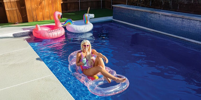 femme se prélassant sur une bouée pailletée avec des bouées licorne dans une piscine de jardin étincelante