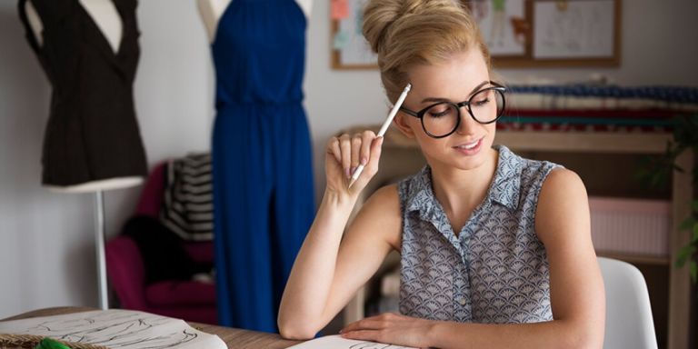 Fashion designer sketching ideas at a desk with mannequins in the background