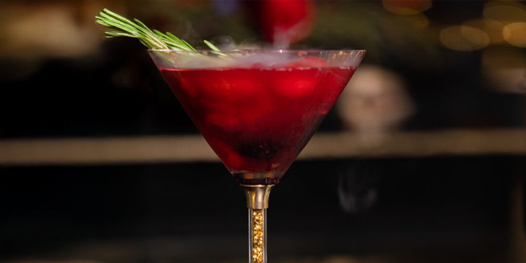 copa de martini de pedrería dorada con líquido rojo en su interior y humo